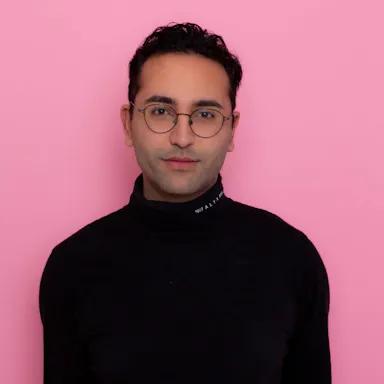 Man, in a black turtleneck shirt, in front of a pink background