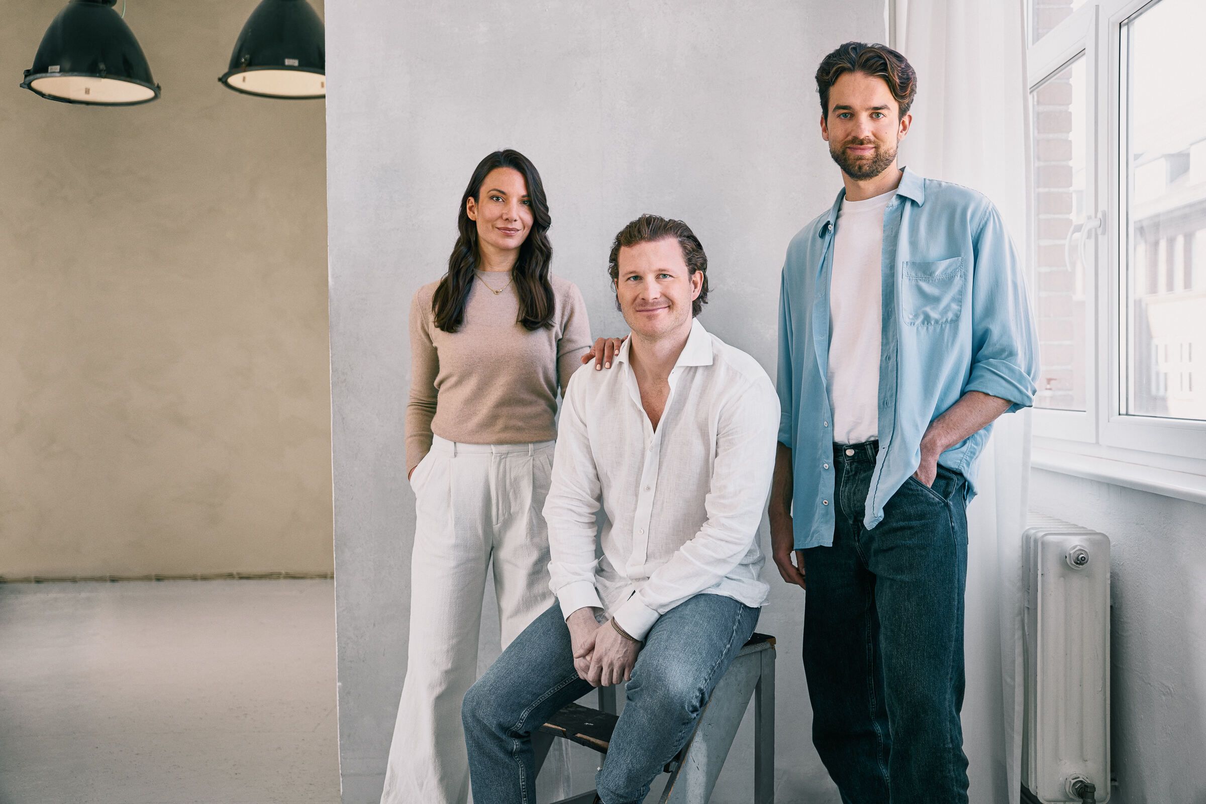 One woman and two men posed against a grey wall