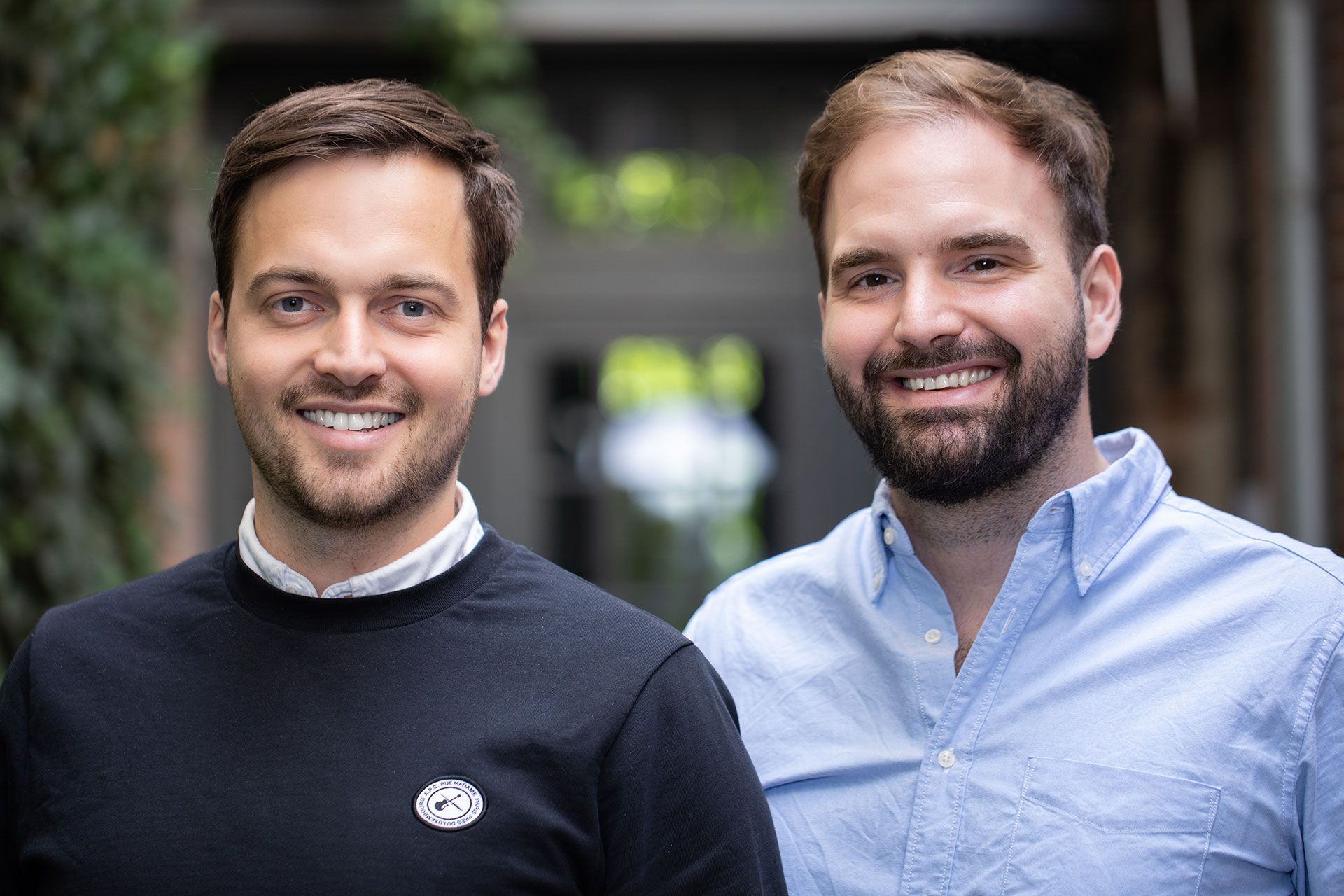 Two men, one in black shirt and one in blue, looking towards the camera