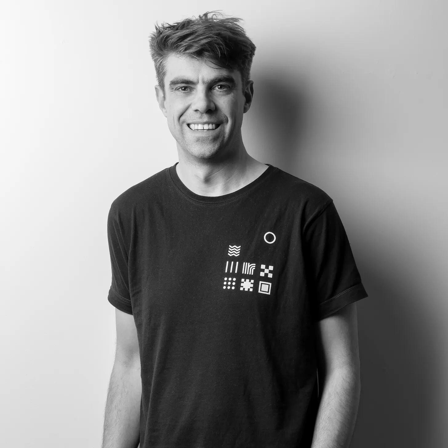 Black and white picture of a man in black shirt, looking towards the camera