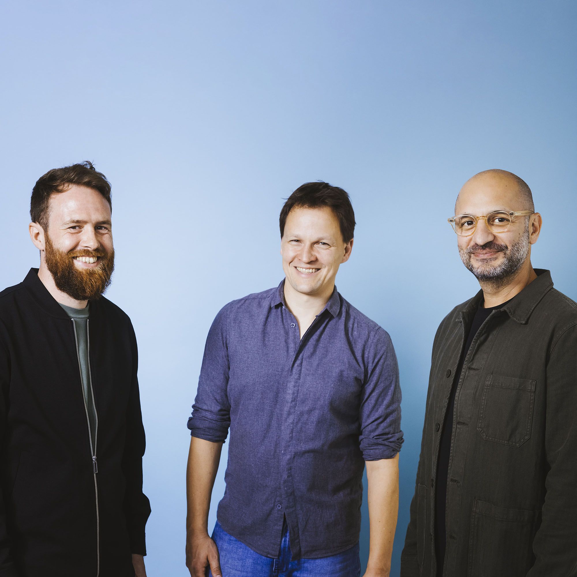 Three men, in front of a blue background, looking at the camera