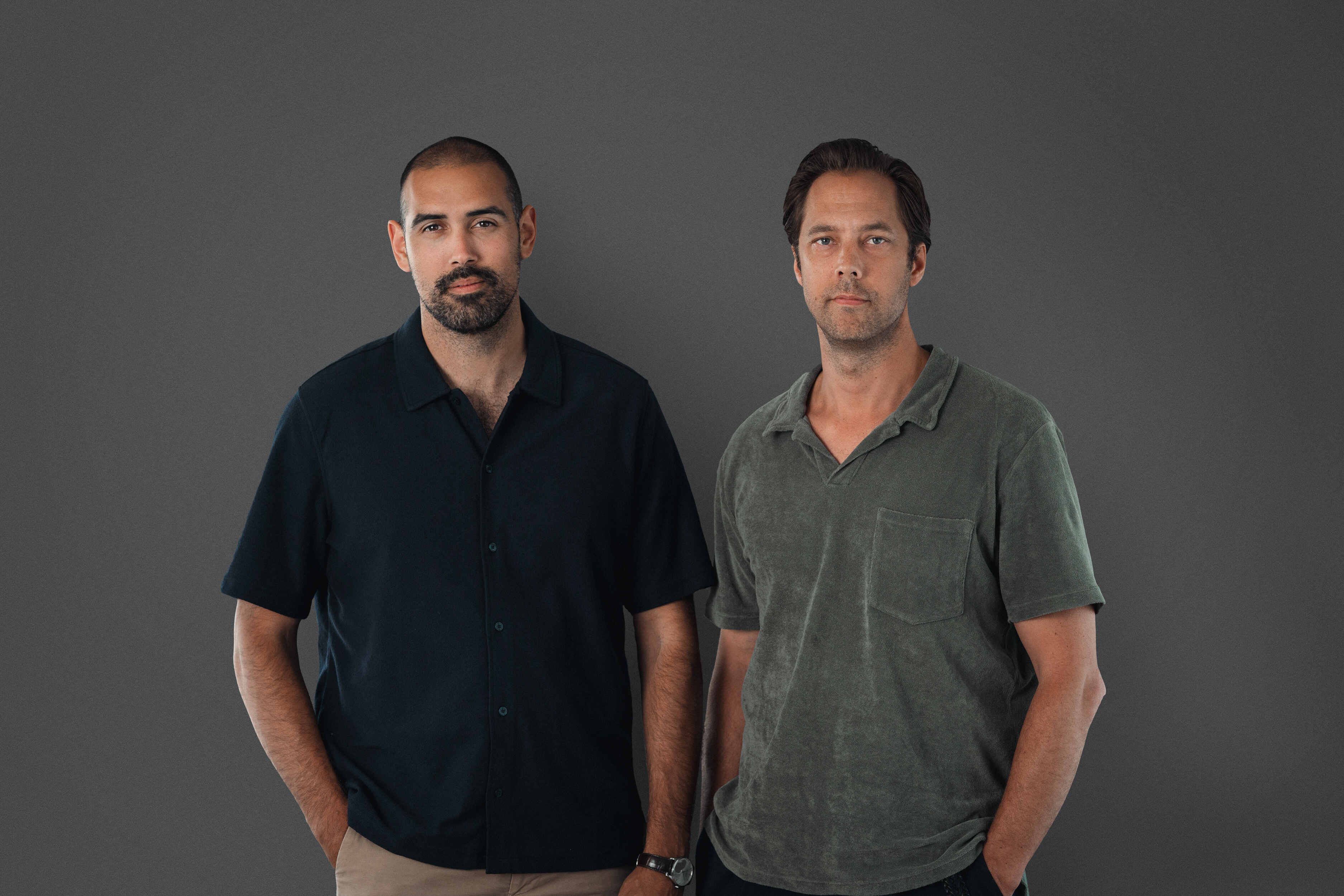 Two men standing against a grey background