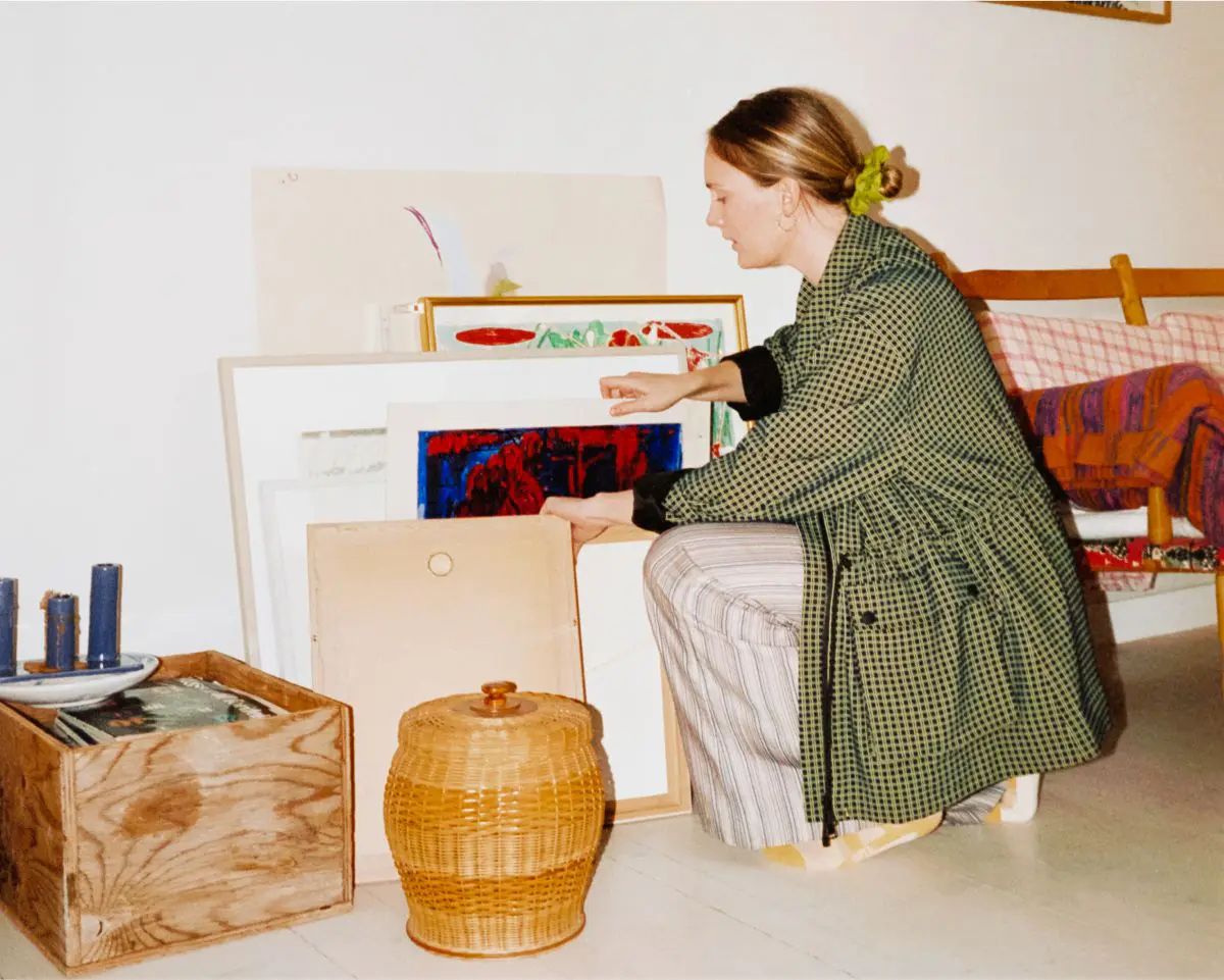 Woman in a living room going through some paintings that are leaning against the wall