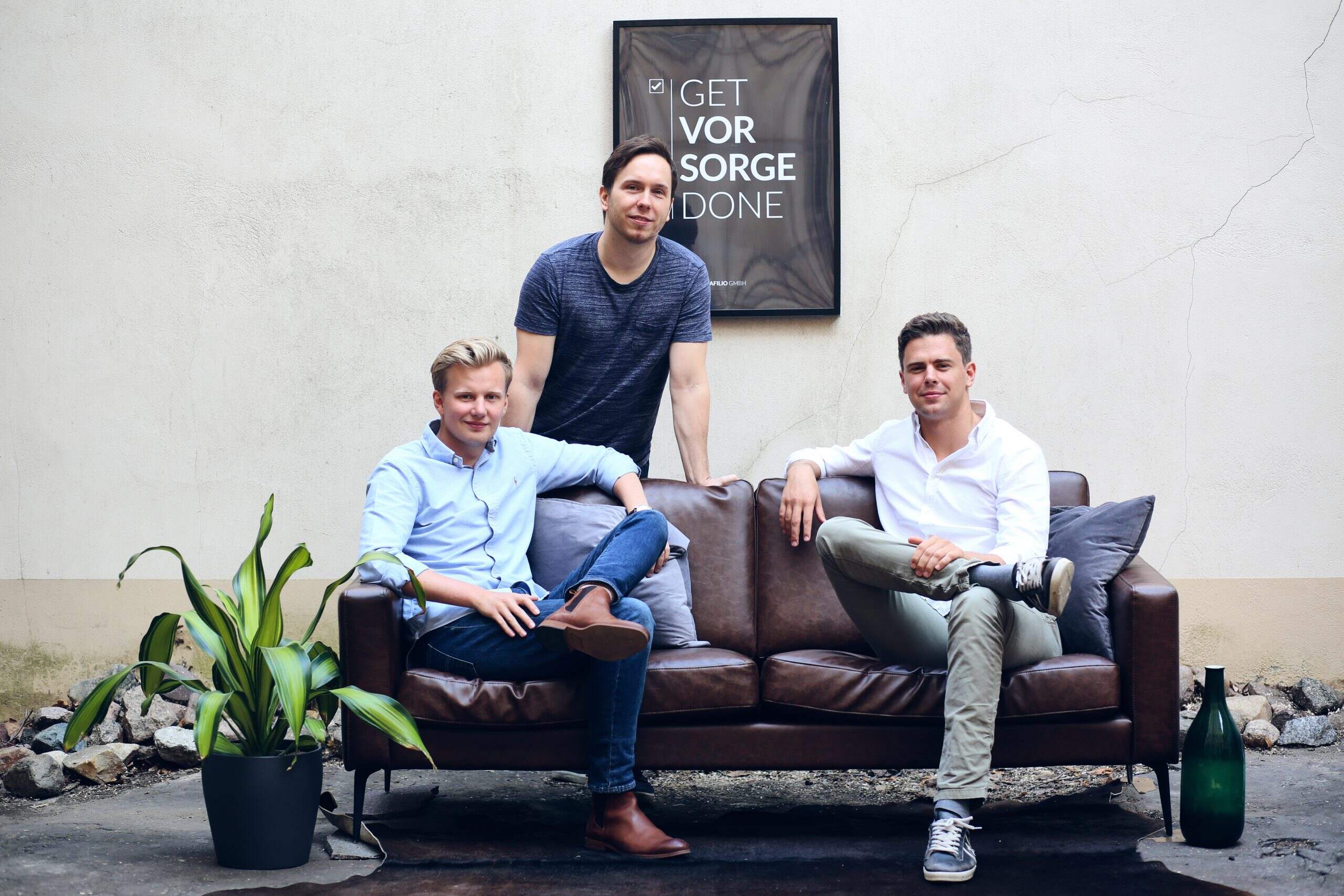 Three men gathered around a brown couch